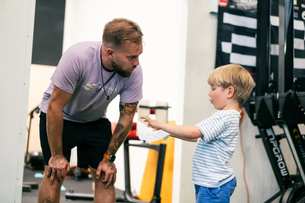 Trener CrossFit Kids rozmawia z chłopcem podczas zajęć