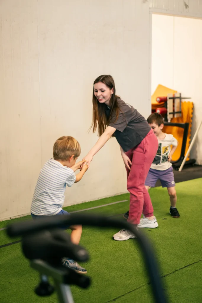 Trenerka trzyma za ręce małego chłopca na zajęciach CrossFit Kids