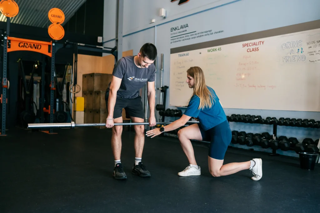 Trener personalny pracuje z klubowiczką przy sztandze