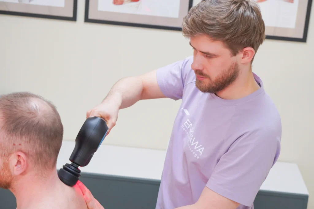 Terapeuta pracuje masażerem perkusyjnym na nodze klienta
