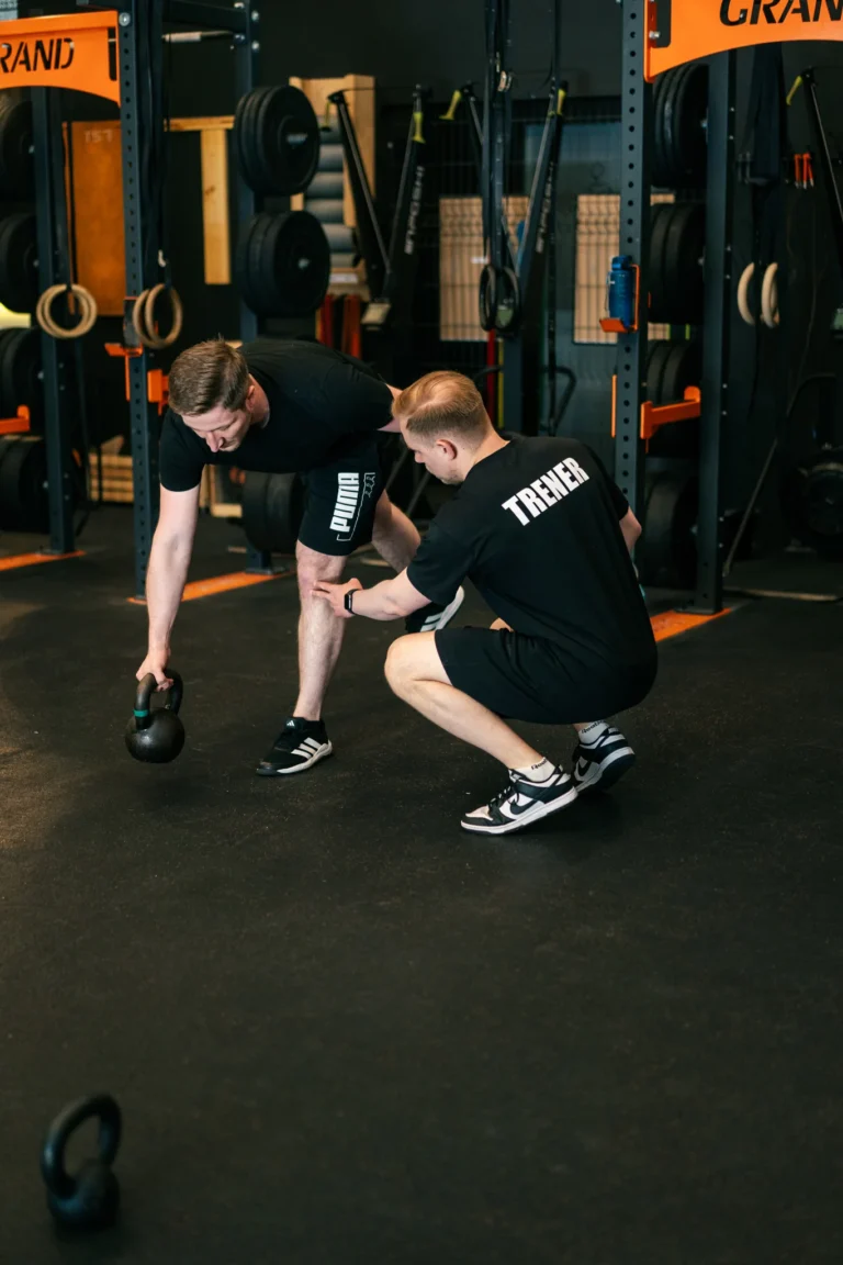 Trener koryguje technikę klienta podczas ćwiczenia z kettlebell